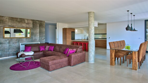 A modern living room with a sectional sofa, a dining table with chairs, and a kitchen in the background. - Aria in Vi Njan With 5 Bedrooms and 4 Bathrooms (Visnjan)