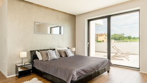 A modern bedroom with a large bed, a nightstand, a mirror, and a view of the outdoors through a sliding glass door. - Aria in Vi Njan With 5 Bedrooms and 4 Bathrooms (Visnjan)