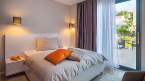 A modern hotel room with a large bed, a nightstand with fruit, and a view of the outdoor patio. - Sunce in Okrug Gornji (Okrug)