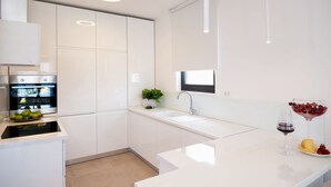 A modern kitchen with white cabinetry, a built-in oven, a sink, and a countertop with a bowl of fruit and a wine glass. - Sunce in Okrug Gornji (Okrug)