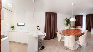 A modern kitchen with white cabinetry, a central island, and a dining area with a round wooden table and white chairs. - Sunce in Okrug Gornji (Okrug)