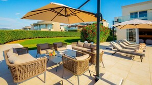 Une terrasse extérieure aménagée avec des meubles en osier, une table garnie de fruits et de boissons, et un espace piscine avec des chaises longues.