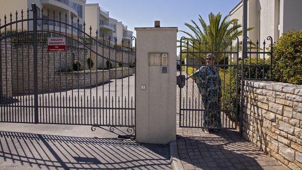 Une entrée fermée par un portail donnant sur un quartier résidentiel, avec une pancarte indiquant qu’il s’agit d’une propriété privée, un coffret électrique et un palmier en arrière-plan.