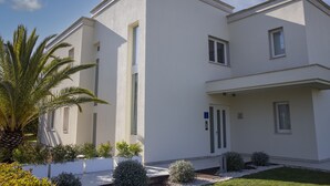 Un bâtiment moderne à deux étages, doté d’un toit plat, de grandes fenêtres et d’un jardin bien entretenu où poussent diverses plantes, ainsi qu’un palmier.