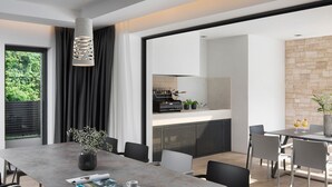 A modern dining area with a large table, chairs, and a vase with flowers. There is a kitchen visible in the background with a stone wall. - Eden in Li Njan With 4 Bedrooms and 4 Bathrooms (Liznjan)