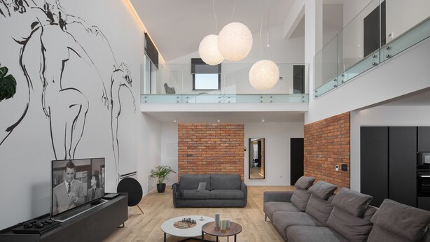 A modern living room with a grey sofa, a coffee table, and a TV. There's a brick wall and a glass railing on the upper level. - Eden in Li Njan With 4 Bedrooms and 4 Bathrooms (Liznjan)