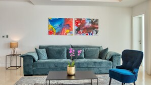 A modern living room with a teal sofa, a blue armchair, and a coffee table. There are abstract paintings on the wall and a lamp on a side table. - Spuga in Brodarica With 4 Bedrooms and 4 Bathrooms (Sibenik)
