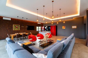 Uma sala de estar moderna com um sofá, uma mesa de centro e cadeiras vermelhas. Na parte de trás, há uma área de cozinha com armários vermelhos e uma mesa de jantar.