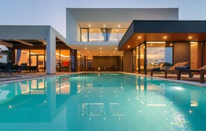 Ett modernt poolområde med ett kristallklart pool, solstolar och en övre våning med glasväggar och fin utsikt.