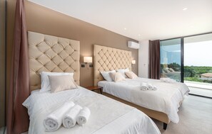 Ett hotellrum med två sängar, ett stort fönster och utsikt över grönområden.