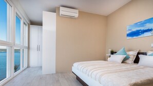 Ein Schlafzimmer mit einem großen Bett, einem Fenster mit Meerblick, einer Deckenklimaanlage und einem Bild an der Wand.