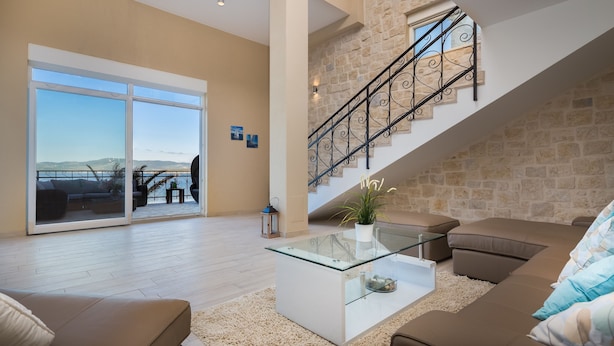 Ein geräumiges Wohnzimmer mit einem Glastisch, einem braunen Sofa und Blick auf einen Balkon mit Geländer.
