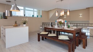 Eine moderne Küche mit einer zentralen Kochinsel, Pendelleuchten und einem Essbereich mit einem Holztisch und Bänken.