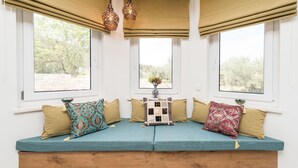 A cozy seating area with a wooden bench and cushioned seats, adorned with patterned cushions, set against a white wall with large windows offering a view of greenery. - Furesta in Tkon Island Pa man (Pasman)