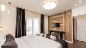 A hotel room with a large bed, a desk with a chair, a TV mounted on a wooden wall, and a door. - Furesta in Tkon Island Pa man (Pasman)