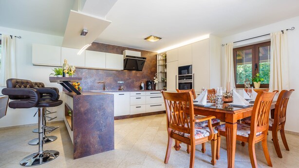 A modern kitchen with a central island, bar stools, and a dining table set for six. - Kamenica in Kras Krk (Dobrinj)