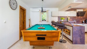 A pool table in a modern kitchen with a clock on the wall, a bar area, and a window with curtains. - Kamenica in Kras Krk (Dobrinj)