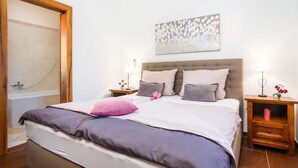 A neatly made bed with a headboard, two bedside tables with lamps, a wooden nightstand, and a wall-mounted artwork. - Kamenica in Kras Krk (Dobrinj)