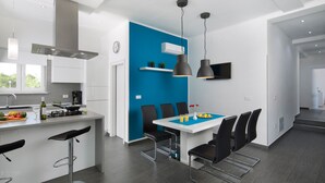 A modern kitchen with white cabinets, a blue accent wall, and a dining area with black chairs and a white table. - Deep Blue in Labin With 3 Bedrooms and 2 Bathrooms (Labin)
