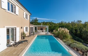 Uma casa moderna com piscina, área de pátio e vista para o verde ao redor.