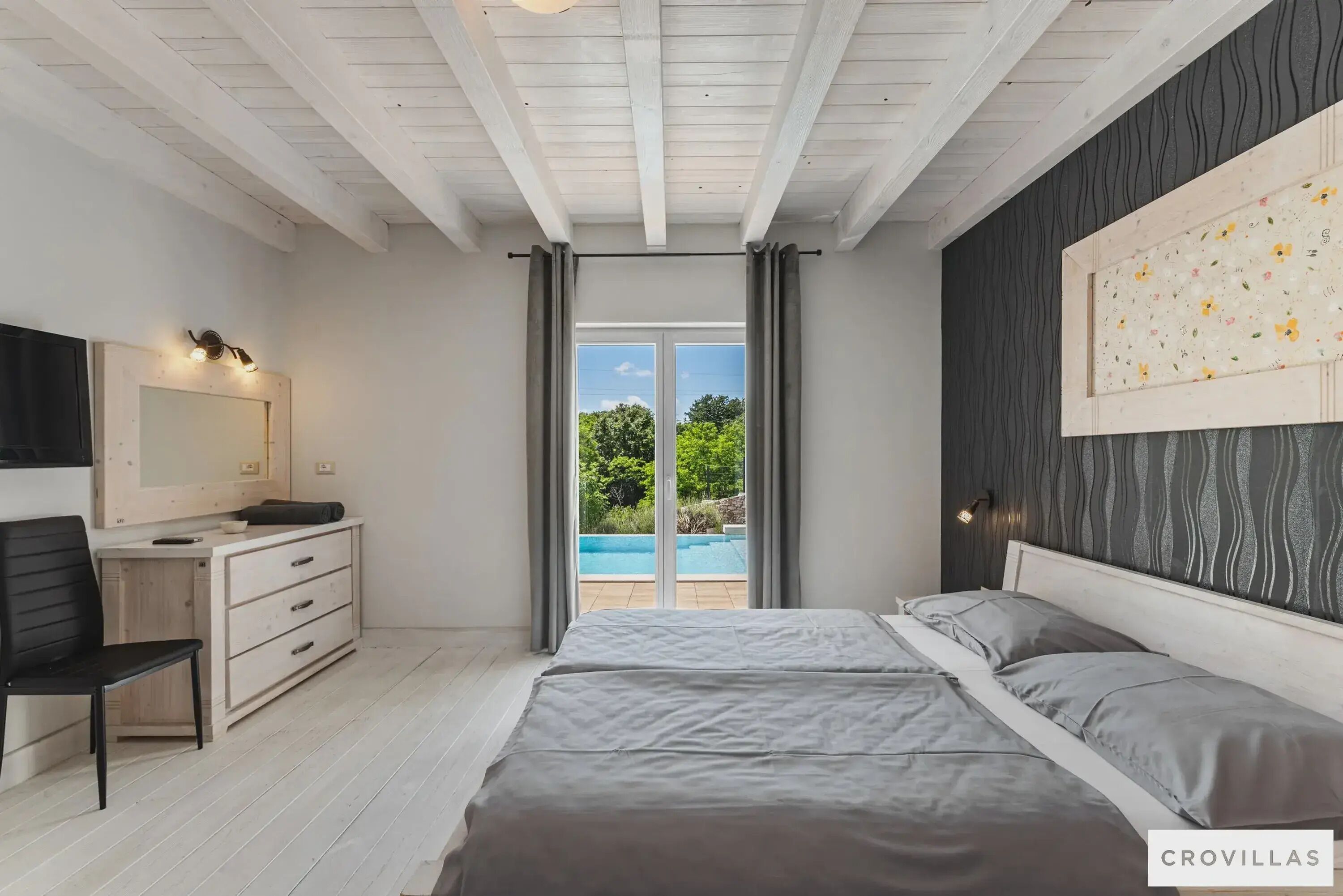 A bedroom with a bed, a dresser, a chair, a mirror, and a view of a swimming pool.