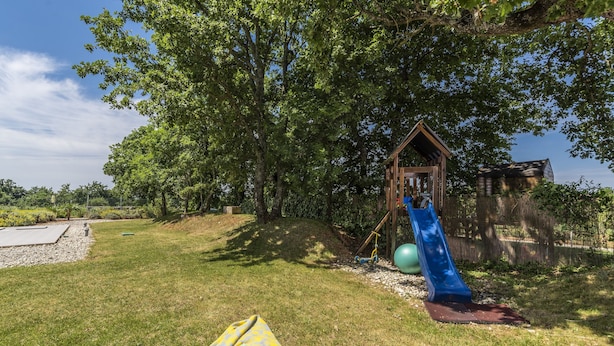 Une aire de jeux avec un toboggan et une balançoire, entourée d’arbres et d’une structure en bois.