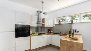 Une cuisine moderne avec des armoires blanches, un four encastré, une hotte de cuisinière en acier inoxydable et un îlot central en bois doté d’un évier et d’un plan de travail.
