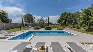 Une piscine rectangulaire à l’eau d’un bleu limpide, entourée d’une terrasse dallée où sont disposés des chaises longues et des serviettes.