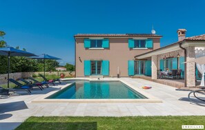 Ein zweistöckiges Haus mit Schwimmbad, Sitzgelegenheiten im Freien und einer Steinterrasse.