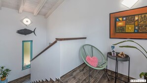 A staircase with a wooden handrail, a green chair with a pink heart cushion, a small table with decorative items, and a framed abstract painting on the wall. - Desire in Jur i i With 4 Bedrooms and 4 Bathrooms (Svetvincenat)