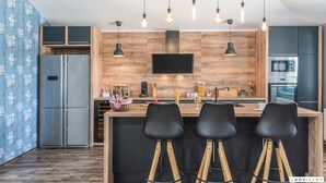 A modern kitchen with wooden accents, a central island with bar stools, a built-in oven, and a flat-screen TV. - Desire in Jur i i With 4 Bedrooms and 4 Bathrooms (Svetvincenat)