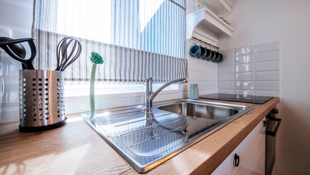 A modern kitchen with a stainless steel sink, wooden countertop, and a window with vertical blinds. - Duzac in Kraj With 2 Bedrooms and 2 Bathrooms (Pasman)