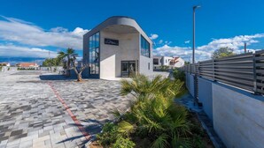 A modern building with a curved roof, a sign reading 'Marc,' and a paved walkway with palm trees. - M3 in Vir With 2 Bedrooms and 2 Bathrooms (Vir)