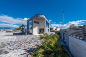 A modern building with a curved roof, a sign reading 'Marc,' and a paved walkway with palm trees. - M3 in Vir With 2 Bedrooms and 2 Bathrooms (Vir)