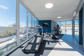 Une salle de sport équipée de tapis de course, de vélos d’appartement et d’un téléviseur fixé au mur.