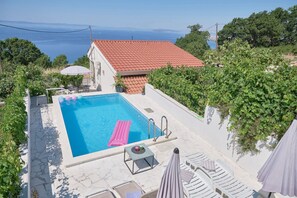 Piscina com cobertura de telhas vermelhas, boia rosa e espreguiçadeiras.