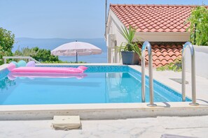 Uma piscina com vista para o mar, um guarda-sol branco e um telhado calado.