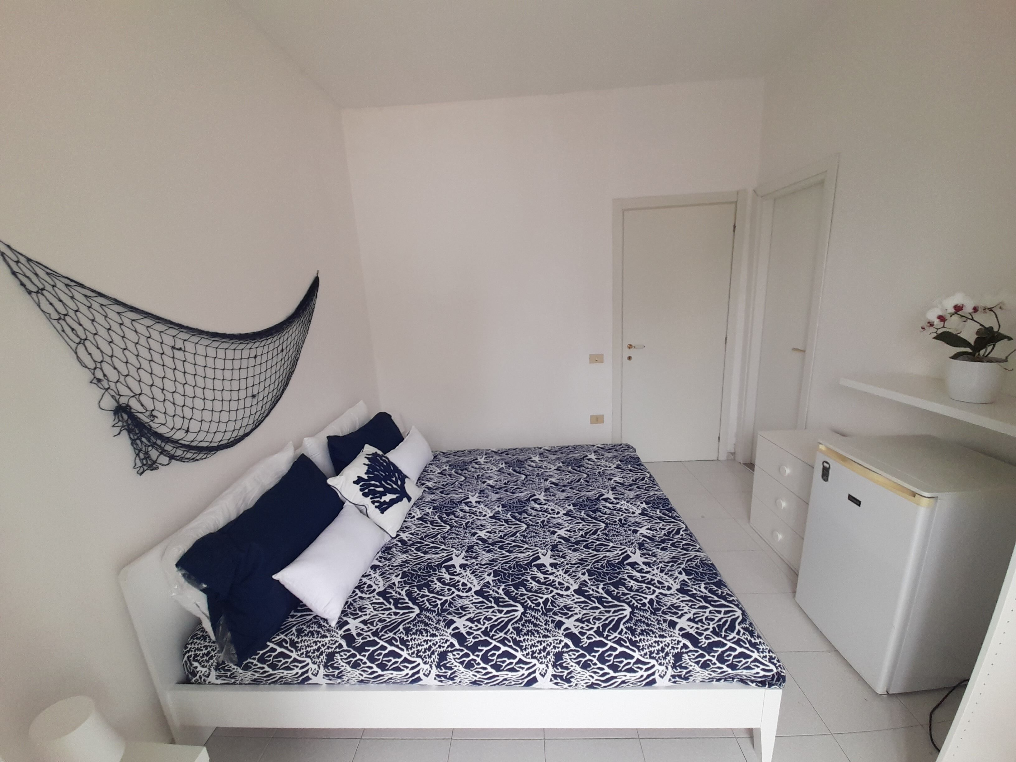 Une chambre à coucher avec un lit, un moustiquaire suspendu, une porte, une commode et une plante en pot.
