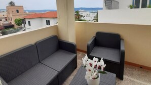 A balcony with two dark grey sofas and a small table with a vase of white flowers. - Exclusive three-bedroom, three-bathroom apartment by the sea at Poetto (CAGLIARI)