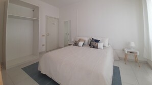 A bedroom with a large bed, a wardrobe, a bedside table, and a mirror. - Exclusive three-bedroom, three-bathroom apartment by the sea at Poetto (CAGLIARI)