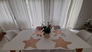 A dining area with a white table, six chairs, star-shaped placemats, and a potted plant with pink flowers. - Exclusive three-bedroom, three-bathroom apartment by the sea at Poetto (CAGLIARI)