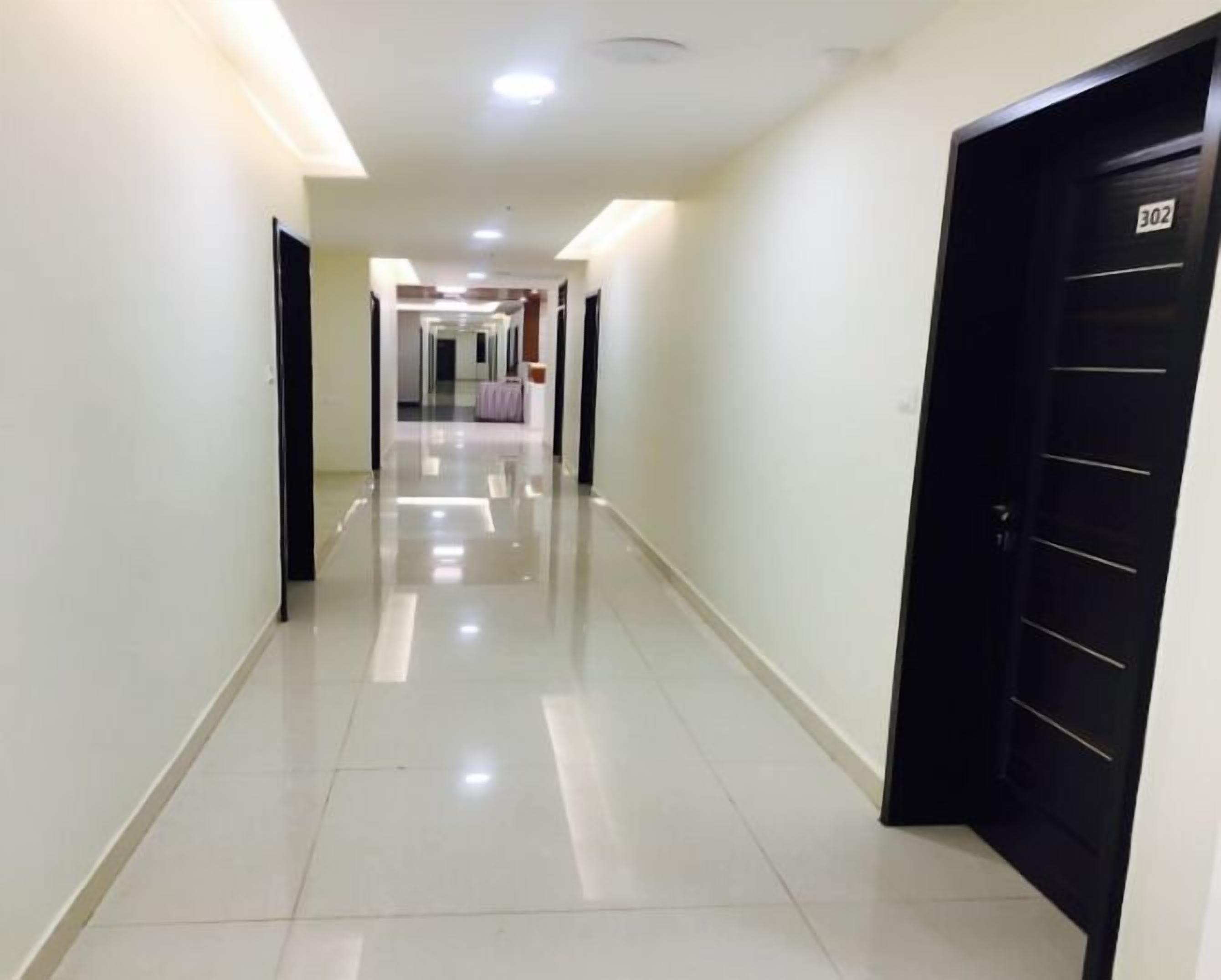Un pasillo de hotel con un suelo de baldosas brillantes, una puerta negra con el número 302 y un accesorio de iluminación en el techo.