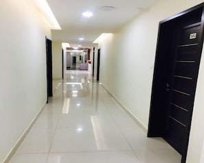 A hotel hallway with a shiny tiled floor, a black door with the number 302, and a light fixture on the ceiling.