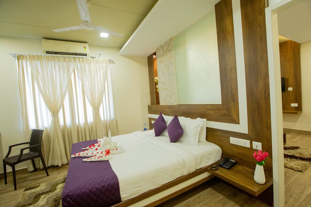 A hotel room with a bed, a chair, a bedside table with a phone, and a vase with flowers.