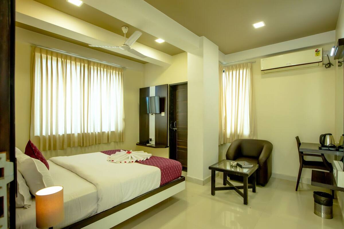 A hotel room with a bed, a desk, a chair, a TV, and an air conditioning unit.