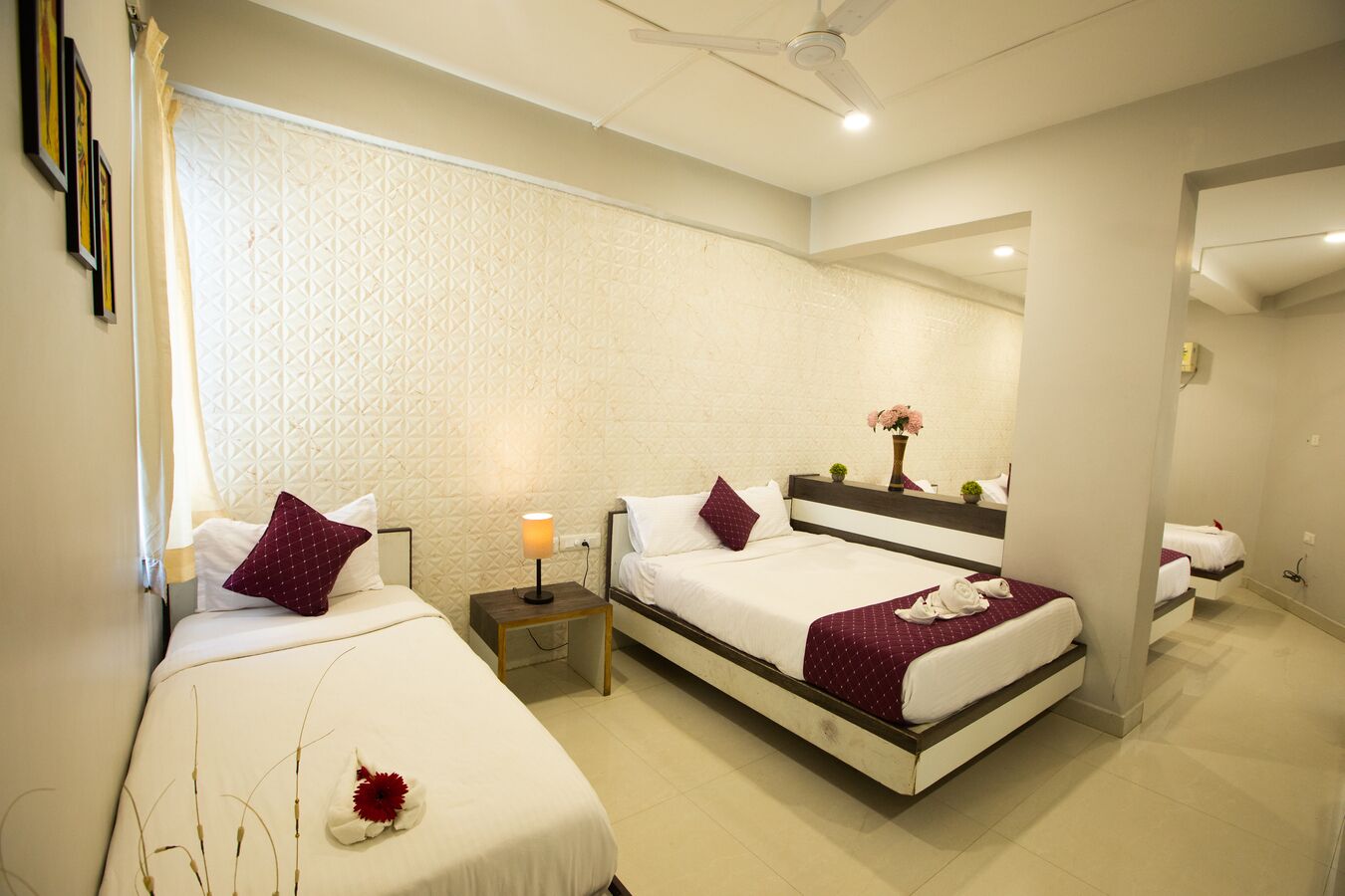 Habitación de hotel con dos camas, una mesita de noche con lámpara, un espejo y un ventilador de techo.