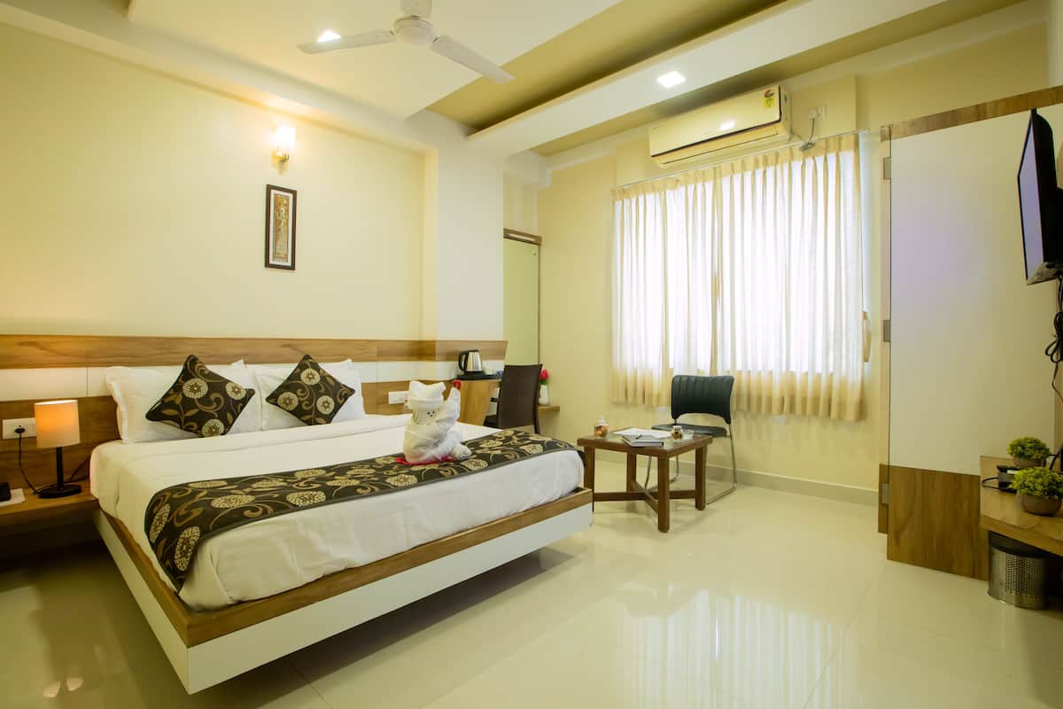A hotel room with a large bed, a desk, a chair, a TV, and a window with curtains.