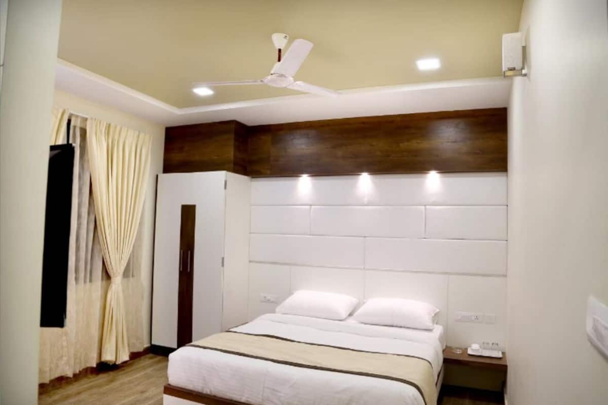 A hotel room with a bed, bedside table, nightstand, curtains, and a ceiling fan.