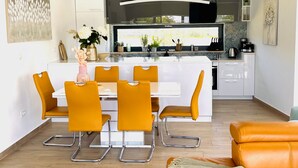 A modern kitchen with white cabinets, a central island with a white countertop, and a dining area with yellow chairs. - Mala Oaza in Sveti Petar u umi (Sveti Petar u Sumi)