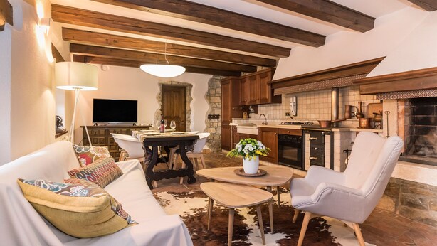Un salon chaleureux avec un canapé, une table à manger et un coin cuisine agrémenté de poutres en bois et de murs en pierre.